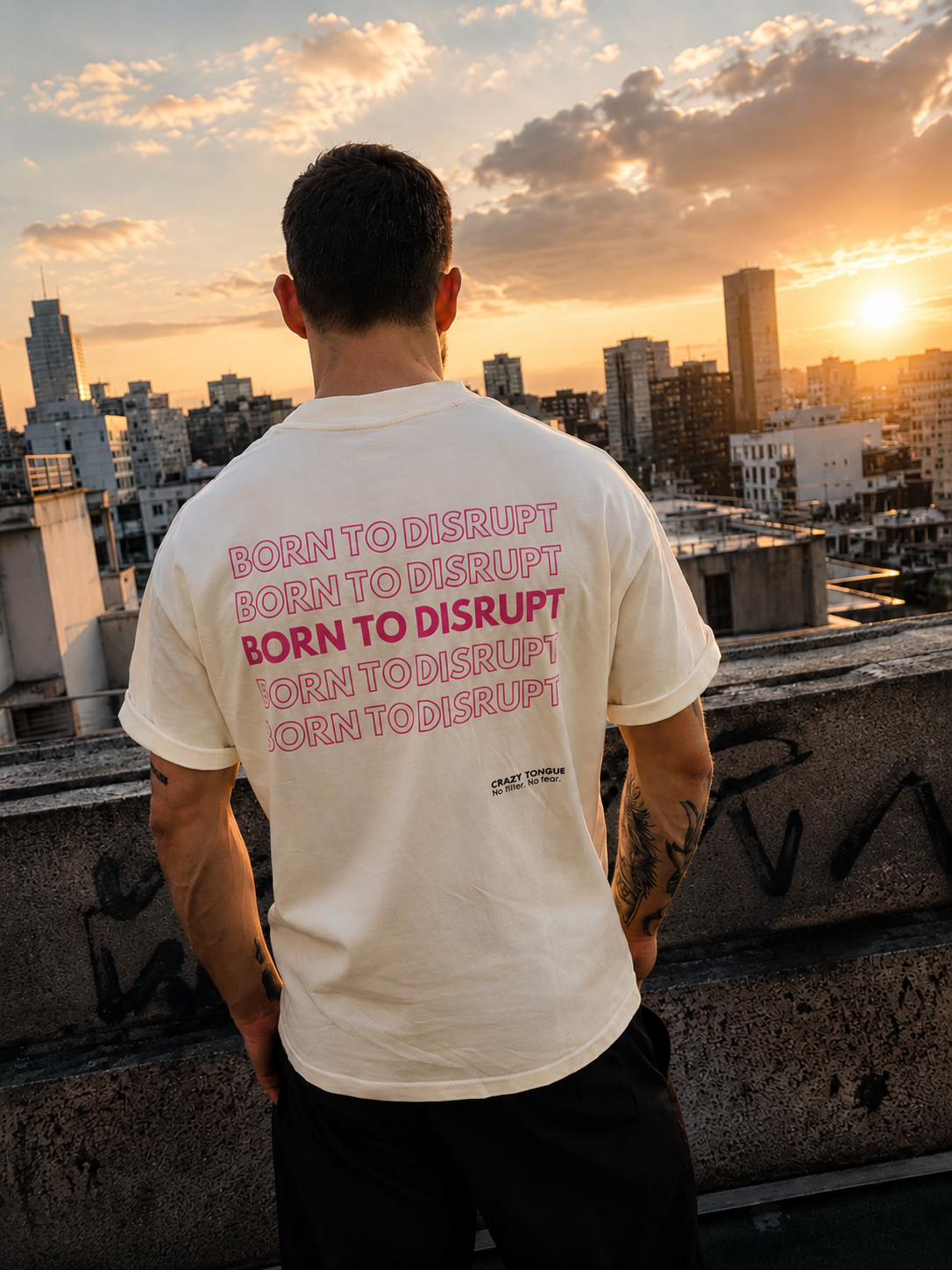 Homme portant le t-shirt crème Crazy Tongue BORN TO DISRUPT de dos sur un rooftop au coucher du soleil.